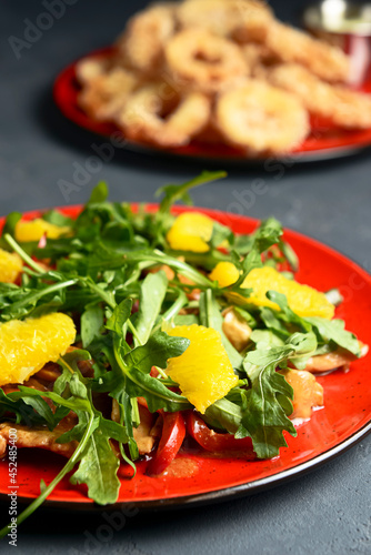 Delicious mixed vegetable and fruit salad served in a red plate over dark background.