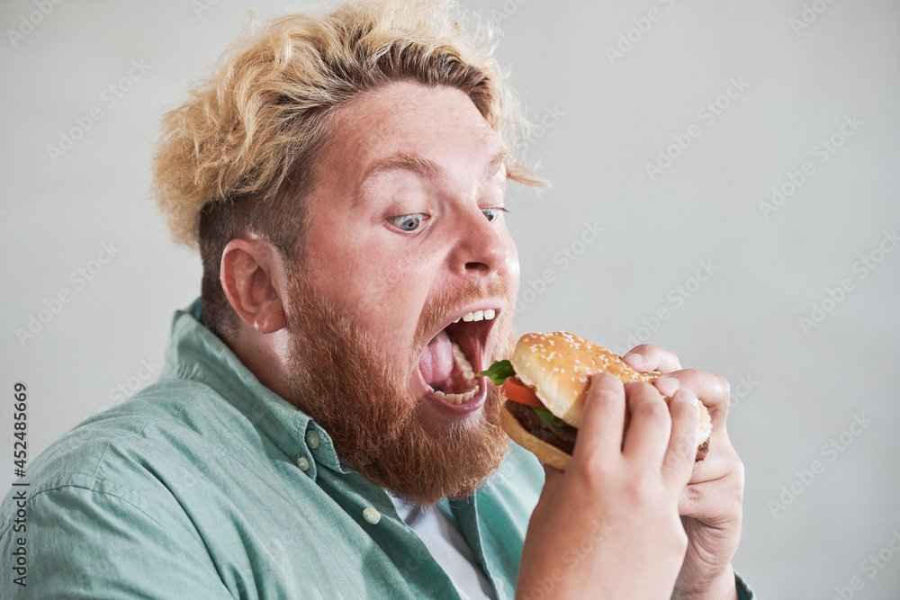 Close-up of overweight man opening his mouth and eating big burger with pleasure isolated on white background Close-up of overweight man opening his mouth and eating big burger with pleasure isolated on white background