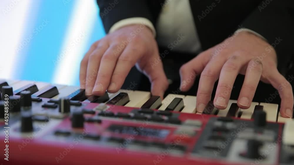 The musician plays a red electronic synthesizer against the background of colored glowing screens. Close-up of the hands of a musician playing an electronic piano at a party. Fingers play on the keys. The musician plays a red electronic synthesizer against the background of colored glowing screens. Close-up of the hands of a musician playing an electronic piano at a party. Fingers play on the keys.