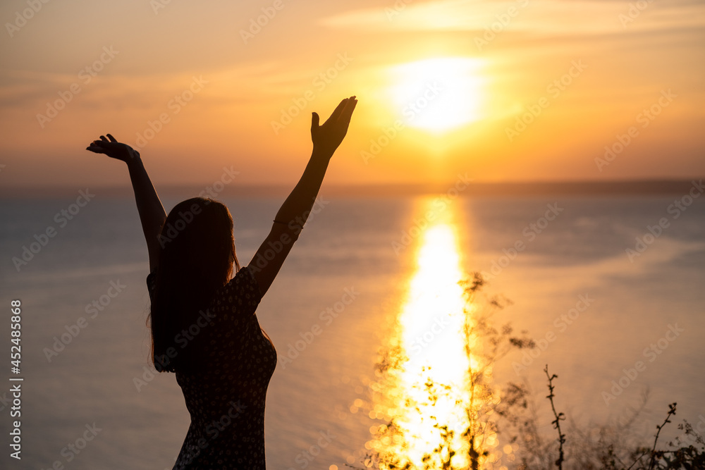 silhouette of a person with arms raised, successful young woman standing in the sunset celebrating success