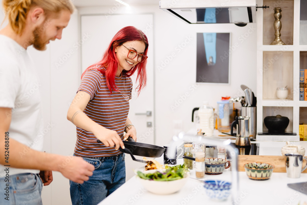 Young white couple smiling while cooking together in kitchen Young white couple smiling while cooking together in kitchen
