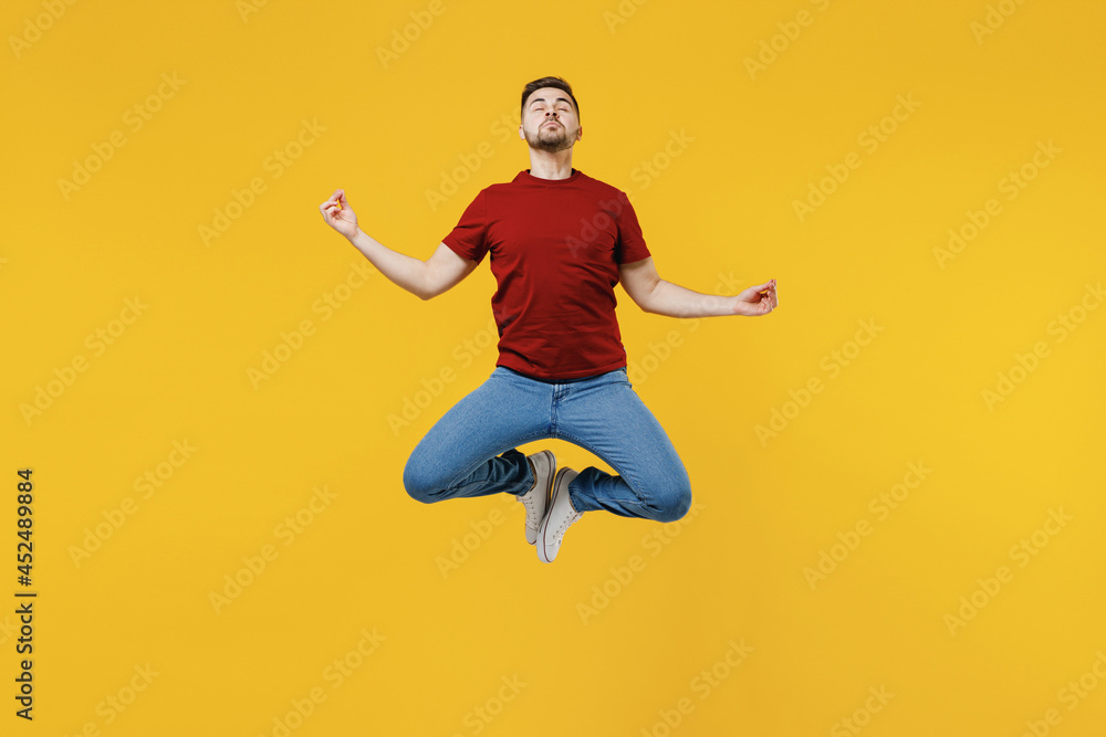 Full length young man 20s in red t-shirt jump high hold spread hand in yoga om aum gesture relax meditate try calm down isolated on plain yellow color wall background studio. People lifestyle concept.