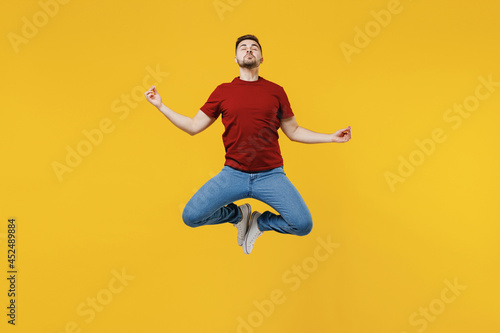 Full length young man 20s in red t-shirt jump high hold spread hand in yoga om aum gesture relax meditate try calm down isolated on plain yellow color wall background studio. People lifestyle concept.