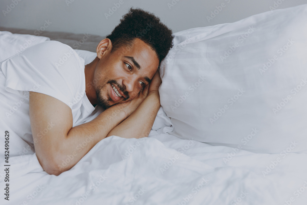 Young minded african american man in nightwear sleep with folded arm under cheek lying in bed rest relax spend time in bedroom lounge home in own room house wake up dream be lost in reverie good day Young minded african american man in nightwear sleep with folded arm under cheek lying in bed rest relax spend time in bedroom lounge home in own room house wake up dream be lost in reverie good day