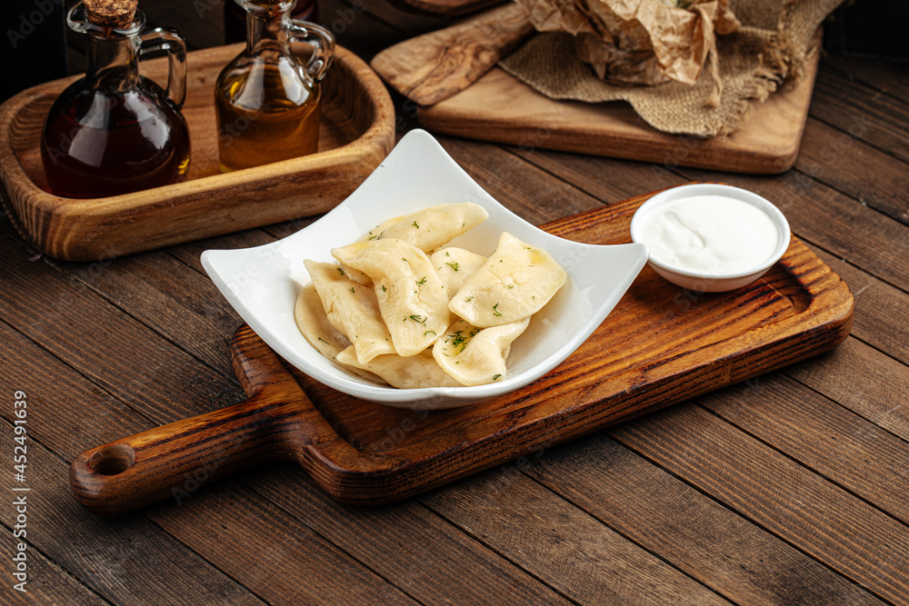 Russian vareniki dumplings with sour cream on wooden background Russian vareniki dumplings with sour cream on wooden background
