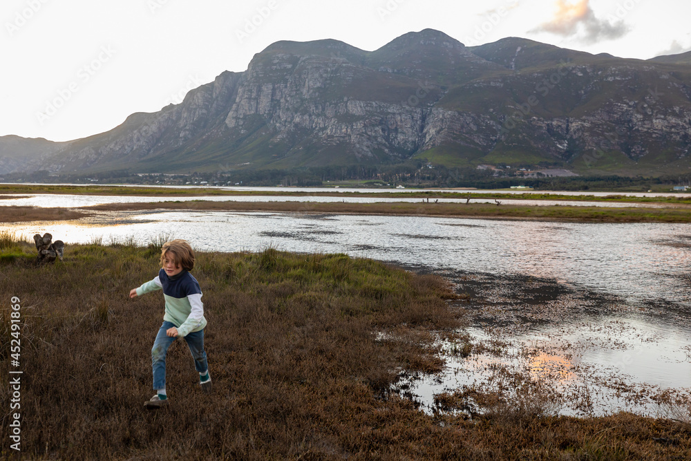 A boy exploring the shore of a lagoon in the shadow of the Kleinriver mountain range A boy exploring the shore of a lagoon in the shadow of the Kleinriver mountain range