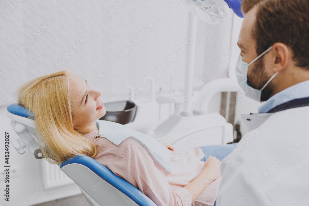Obraz premium Young side view smiling calm fun happy woman 20s with dental napkin sit at dentist office chair indoor light modern cabinet near stomatologist wait for oral procedure Healthcare oral enamel treatment.