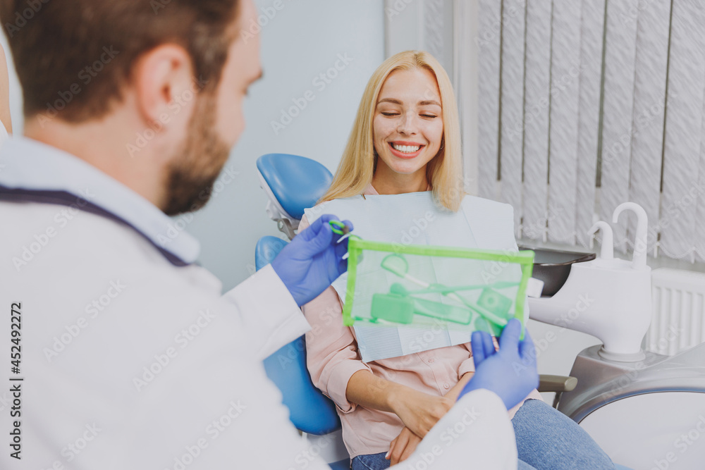 Obraz premium Close up stomatologist young man doctor wear gown give kit care braces grooming brushes for cleaning to patient caucasian woman sitting at dentist office chair indoor cabinet. Healthcare treatment