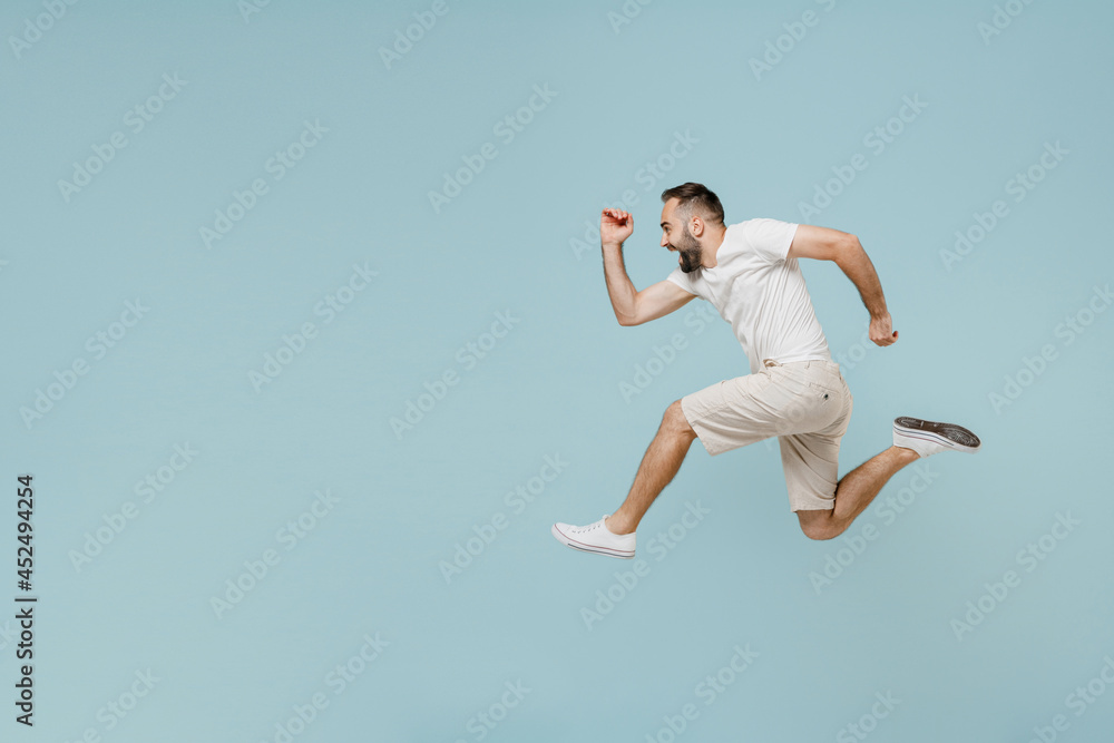 Full length side view young excited happy sportsman caucasian man 20s wearing casual white t-shirt jump high run fast hurrying up isolated on plain pastel light blue color background studio portrait