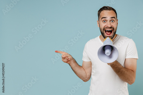 Young happy man in white t-shirt hold scream in megaphone announces discounts sale Hurry up point index finger aside on workspace area isolated on plain pastel light blue background studio portrait