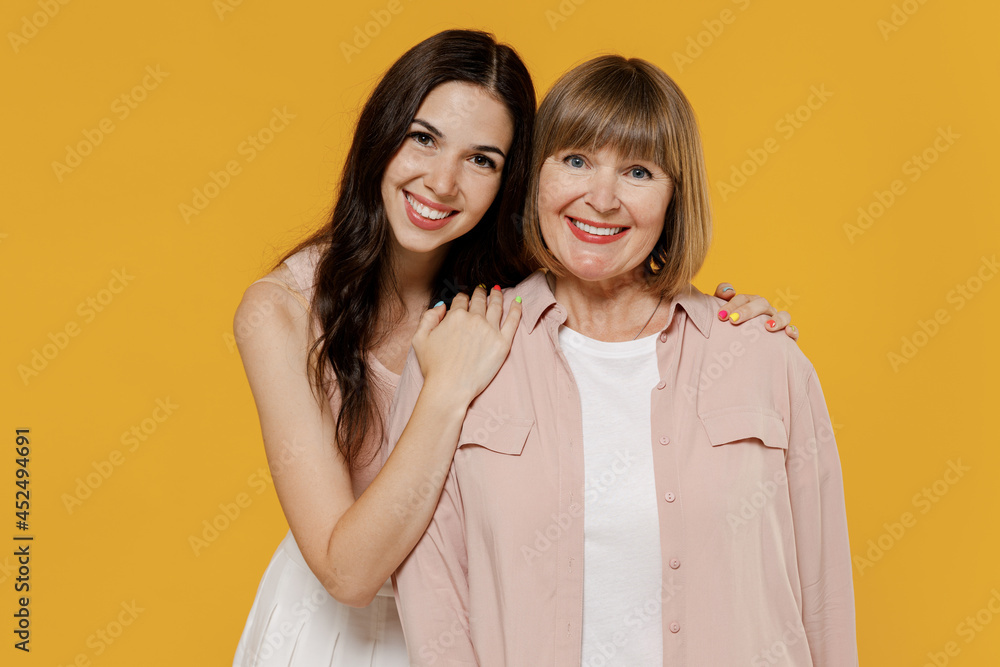 Two young smiling happy daughter mother together couple women wearing casual beige clothes looking camera hugging isolated on plain yellow color background studio portrait. Family lifestyle concept. Two young smiling happy daughter mother together couple women wearing casual beige clothes looking camera hugging isolated on plain yellow color background studio portrait. Family lifestyle concept.