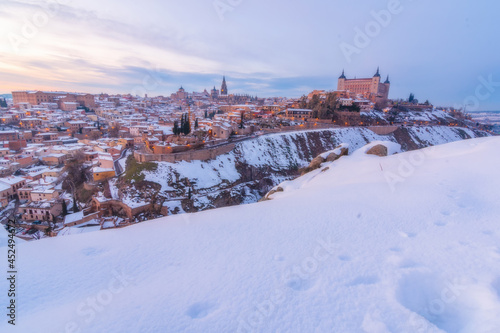 Sunset landscape of snowy old city with colorful clouds and snow; Cathedral and Alcazar of Toledo in storm Filomena, World Heritage Site, Spain. Horizontal view 