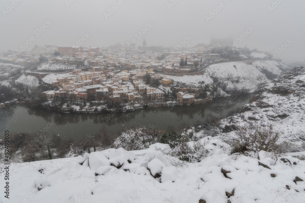 City landscape of snowy old city with clouds and snow; Cathedral and Alcazar of Toledo during the storm Filomena, World Heritage Site, Spain. Horizontal view City landscape of snowy old city with clouds and snow; Cathedral and Alcazar of Toledo during the storm Filomena, World Heritage Site, Spain. Horizontal view