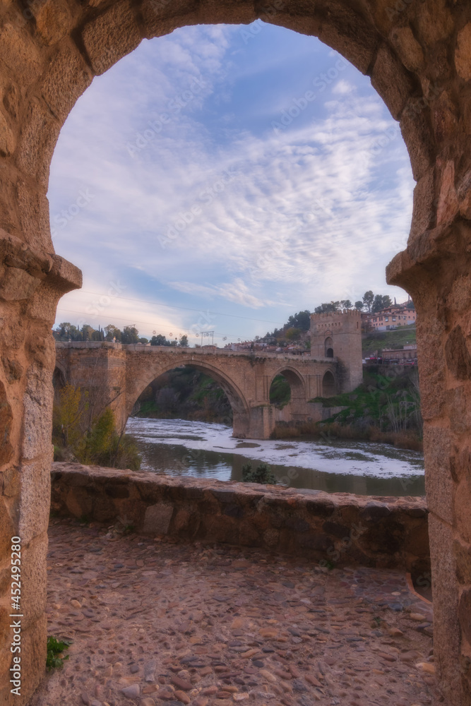 Landscape at sunset of stone bridge over Tajo river in old city with colorful clouds at sunset; San Martin Bridge in Toledo, World Heritage Site, Spain. vertical view