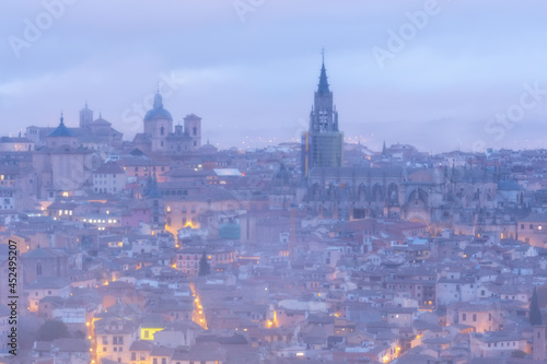 Cityscape in old city changing light at dawn  Tower of the primate cathedral with the old town and its small streets of Toledo with fog and clouds  world heritage site  Spain. Horizontal view