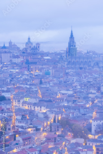 Cityscape in old city changing light at dawn; Tower of the primate cathedral with the old town and its small streets of Toledo with fog and clouds, world heritage site, Spain. Vertical view