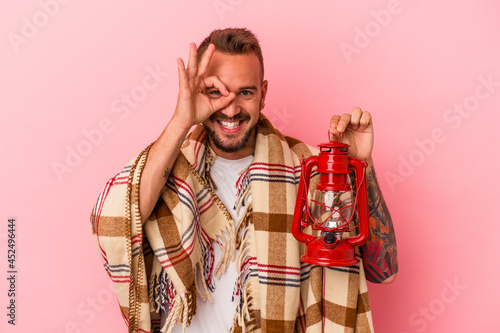 Young caucasian man with tattoos holding vintage lantern isolated on pink background excited keeping ok gesture on eye.