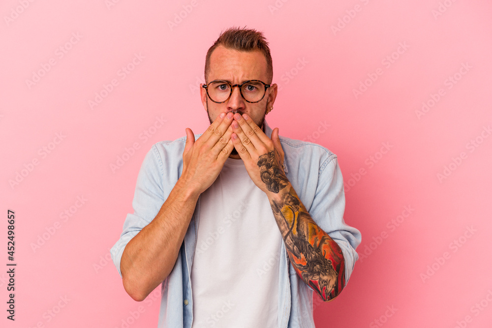 Young caucasian man with tattoos isolated on pink background shocked, covering mouth with hands, anxious to discover something new. Young caucasian man with tattoos isolated on pink background shocked, covering mouth with hands, anxious to discover something new.