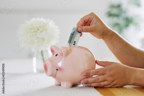 A woman put a euro note in a piggy bank photo