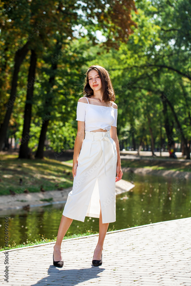 Young beautiful brunette girl in a white skirt posing in a summer park Young beautiful brunette girl in a white skirt posing in a summer park