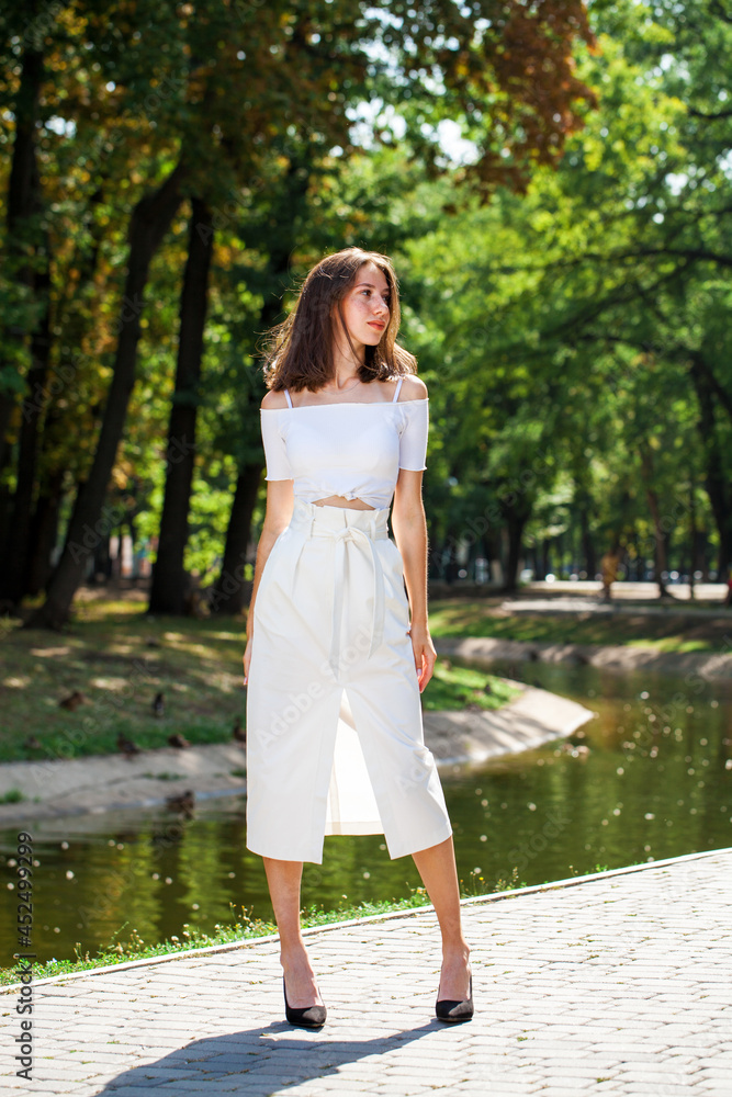 Young beautiful brunette girl in a white skirt posing in a summer park Young beautiful brunette girl in a white skirt posing in a summer park