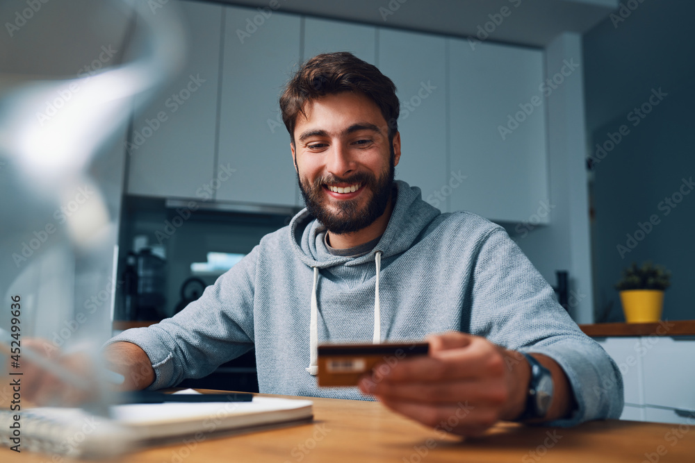 Smiling young man making online payments at home with credit card and laptop Smiling young man making online payments at home with credit card and laptop