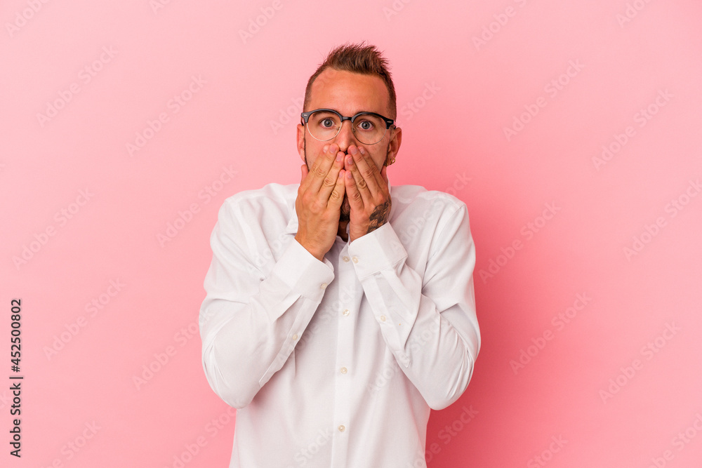 Young caucasian man with tattoos isolated on pink background shocked, covering mouth with hands, anxious to discover something new. Young caucasian man with tattoos isolated on pink background shocked, covering mouth with hands, anxious to discover something new.