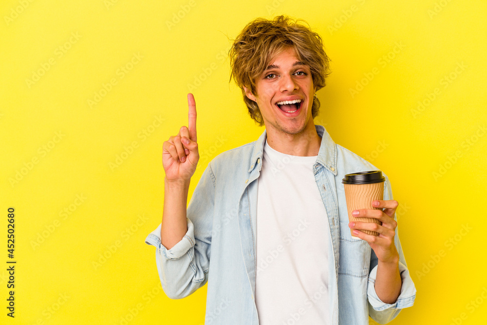 Young caucasian man with makeup holding a take away coffee isolated on yellow background showing number one with finger. Young caucasian man with makeup holding a take away coffee isolated on yellow background showing number one with finger.