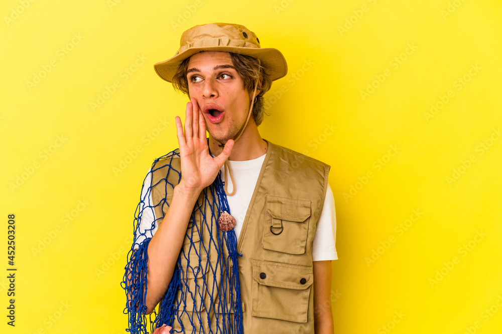 Young fisherman with makeup holding a net isolated on yellow background is saying a secret hot braking news and looking aside Young fisherman with makeup holding a net isolated on yellow background is saying a secret hot braking news and looking aside