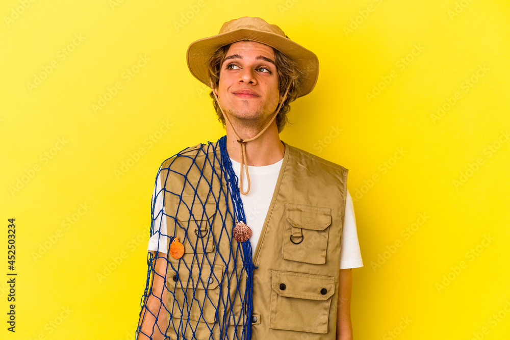 Young fisherman with makeup holding a net isolated on yellow background dreaming of achieving goals and purposes Young fisherman with makeup holding a net isolated on yellow background dreaming of achieving goals and purposes