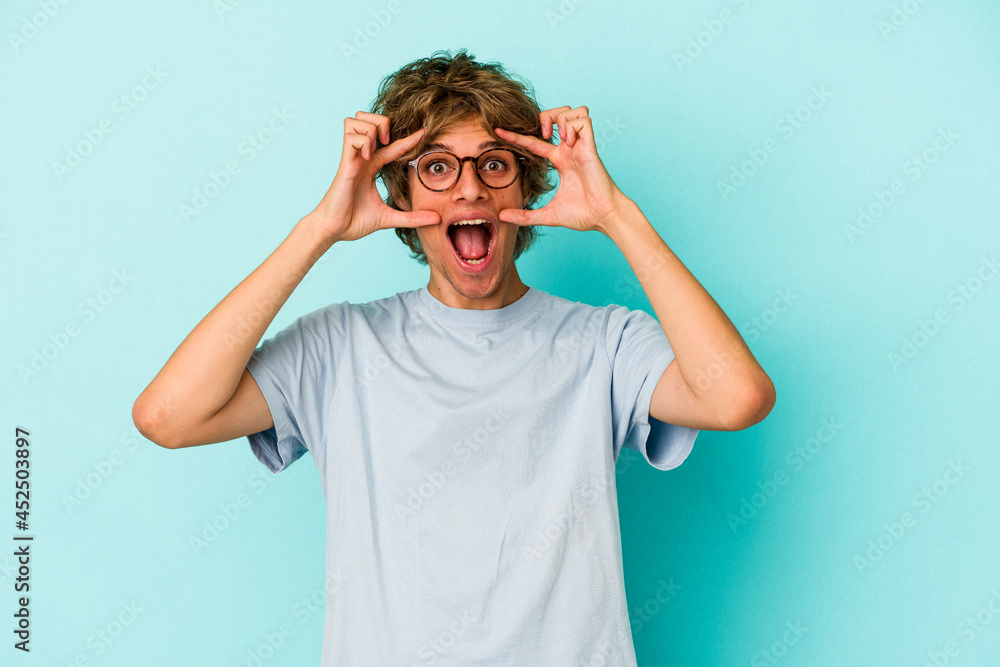 Young caucasian man with make up isolated on blue background keeping eyes opened to find a success opportunity. Young caucasian man with make up isolated on blue background keeping eyes opened to find a success opportunity.