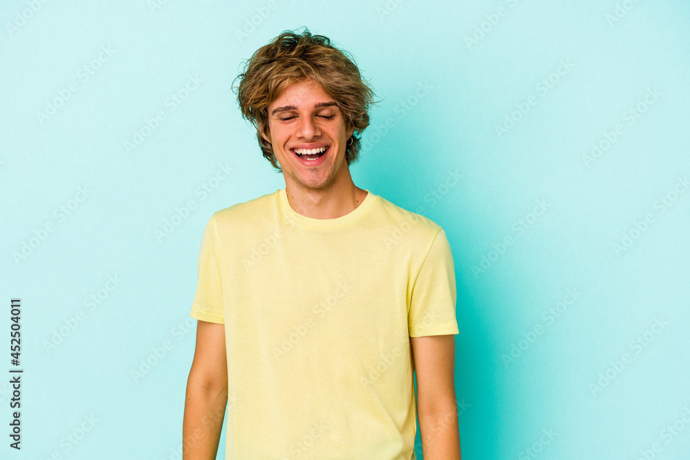 Young caucasian man with make up isolated on blue background laughs and closes eyes, feels relaxed and happy. Young caucasian man with make up isolated on blue background laughs and closes eyes, feels relaxed and happy.