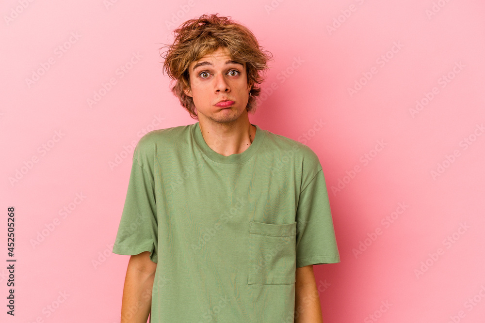 Young caucasian man with make up isolated on pink background shrugs shoulders and open eyes confused. Young caucasian man with make up isolated on pink background shrugs shoulders and open eyes confused.
