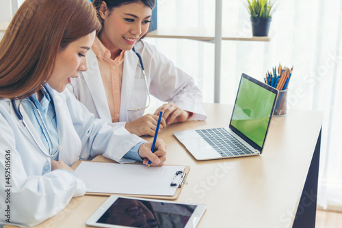 Two asian women doctors discuss meeting doctor's office medical clinic using laptop consulting patient disease. Asian medical lab young women talking together discussing healthcare assistance teamwork