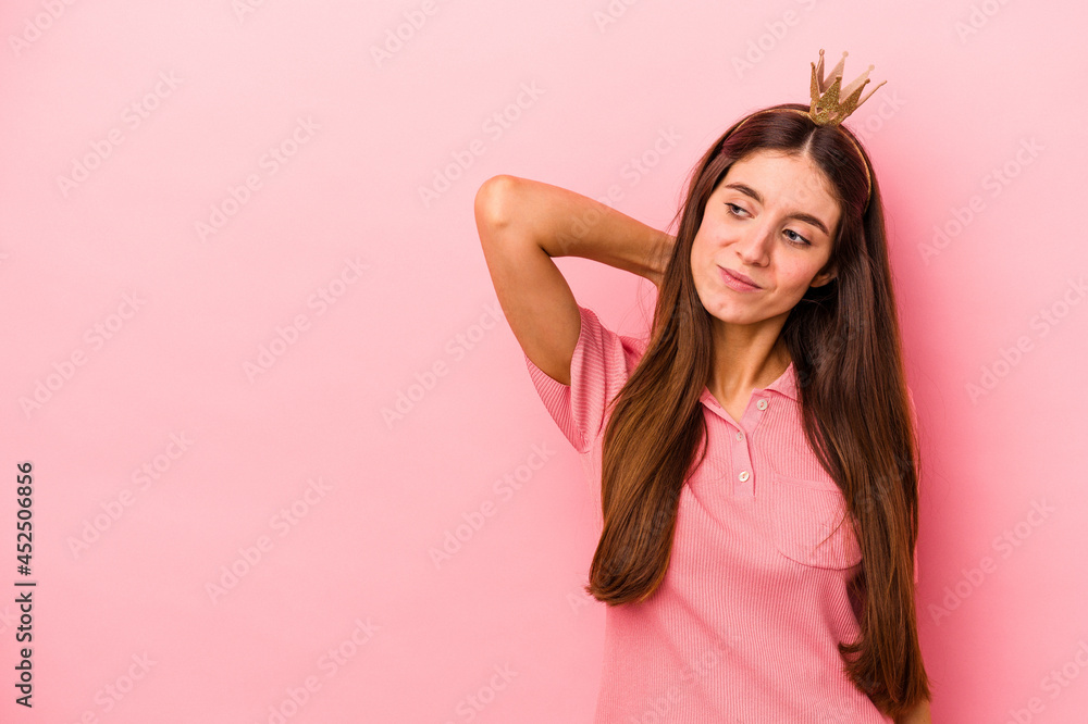 Young caucasian woman wearing crown isolated on pink background touching back of head, thinking and making a choice. Young caucasian woman wearing crown isolated on pink background touching back of head, thinking and making a choice.