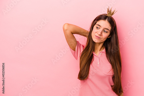 Young caucasian woman wearing crown isolated on pink background touching back of head, thinking and making a choice.