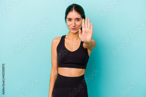 Young sporty caucasian woman isolated on blue background standing with outstretched hand showing stop sign, preventing you.