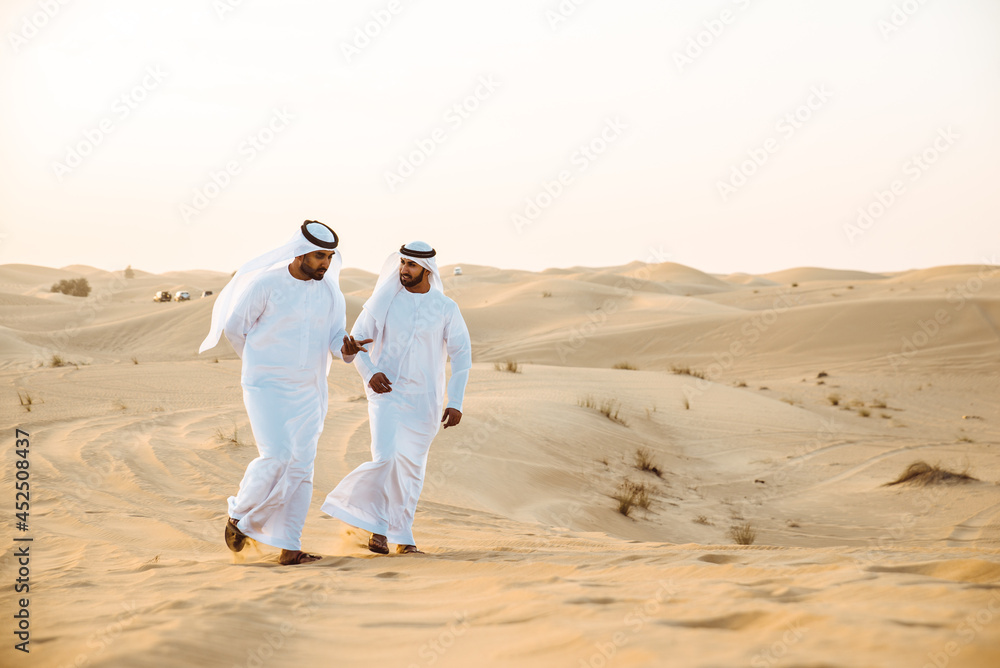 Naklejka premium Two business men wearing traditional uae white kandura spending time in the desert of Dubai