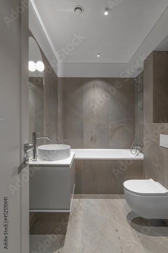 Modern minimalist bathroom beige interior design with marble tiles and beige furniture.