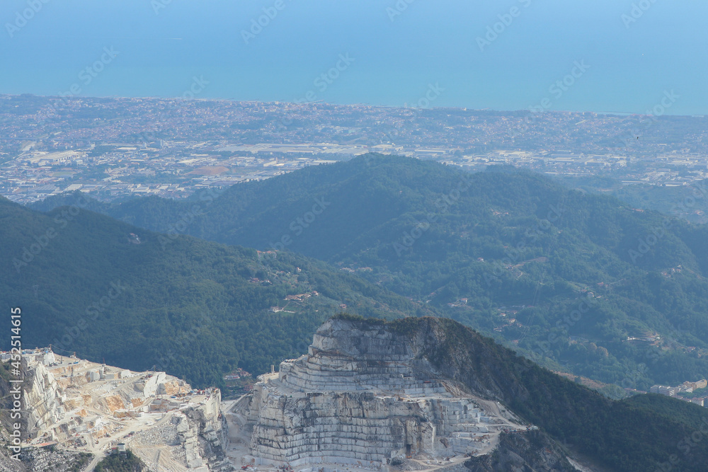 Panorama con cava di marmo di Carrara, Alpi Apuane, città sulla costa e mar Mediterraneo.