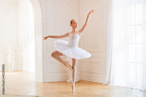 Leinwand Poster young slender ballerina in a white tutu in pointe shoes is dancing in large beautiful white hall