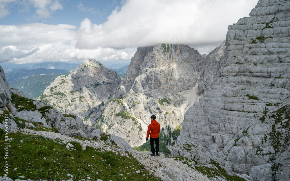 Fototapeta premium Active male hiker enjoying the view. Hiking man adventure travel explorer hiker on mountain summit looking at landscape view. Adventure, Explore and Lifestyle Concept Composite. Alpi Giulie