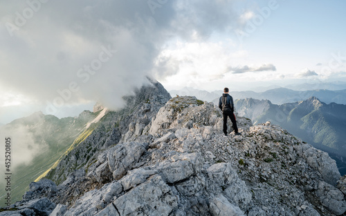 A hiker stands on the ridge watching the valley being flooded by clouds at sunset. Traveling in mountains. Adventure, Art, Travel and Hike concept.