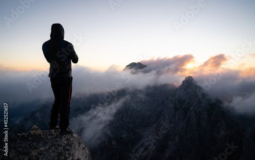 Climber ascent. Scenic landscape photo composite. Man on top of a mountain watching the colorful sunset. Traveller photographing the beautiful nature scenics with smartphone while on vacation