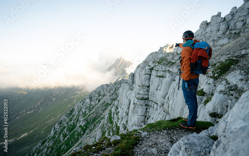Man with backpack high above the misty mountain valley. Lone person looks onwards at a mountain shrouded in mist and clouds with the peak visible. Scenic landscape photo composite.