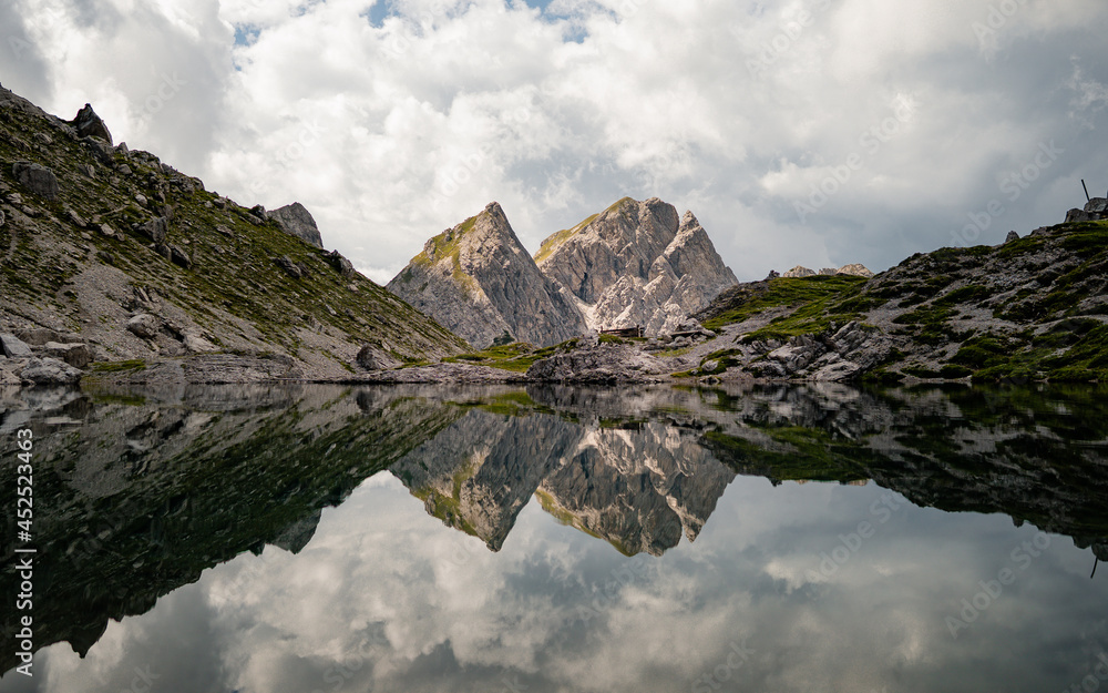 Valley with a small lake in the middle, located between sharp and stony mountain range of Lienz Dolomites (Karlsbader Hutte) Austria. The slopes are barren, with little grass on it. Dangerous mountai