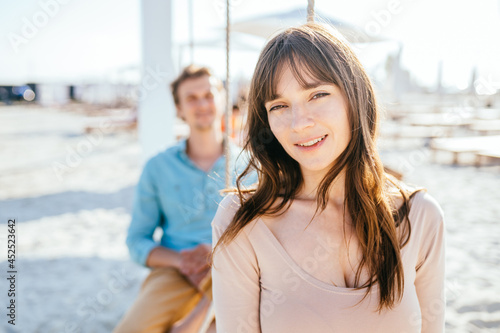 Close up of beautiful caucasian woman and man sitting on swings at the seashore. Summer holidays, love, relaxing concept.