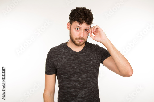 Photography Serious dark-haired caucasian young man touching one eye with his bearded hand l