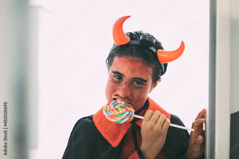 Φωτογραφία Girl in devil costume taking a bite out of a colorful lollipop at the door of a