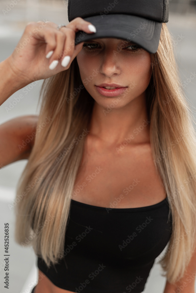 Young pretty hipster woman in fashion black clothes straightens black cap on the street, close-up Young pretty hipster woman in fashion black clothes straightens black cap on the street, close-up
